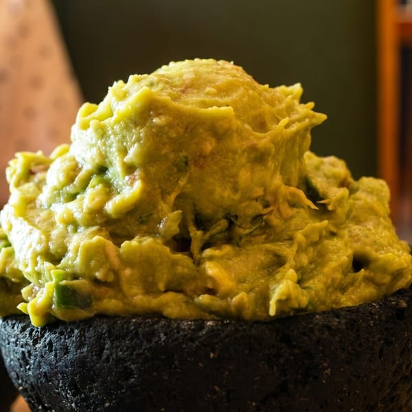 Fresh chunky guacamole piled in a black stone molcajete on a restaurant table.