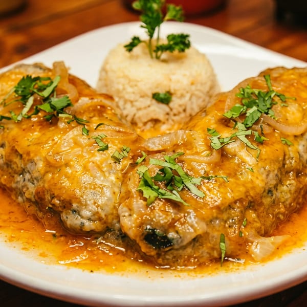 Three meatloaf portions topped with onion gravy and cilantro, served with a mound of rice on a white plate.
